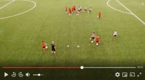 meinkarrierestart.at Eine Gruppe von Kindern und ein Trainer sind während einer Übung auf einem Fußballfeld, wobei einige Spieler Bälle dribbeln und andere sich im Hintergrund versammelt haben.