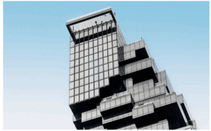 meinkarrierestart.at Modernes Glasgebäude mit unregelmäßigem, gestapeltem Design vor einem klaren blauen Himmel.