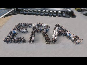 meinkarrierestart.at Eine große Gruppe von Menschen steht in Formation auf dem Bürgersteig und bildet die Form eines Pfeils, der nach rechts zeigt. Im Hintergrund sind mehrere Fahrzeuge geparkt.