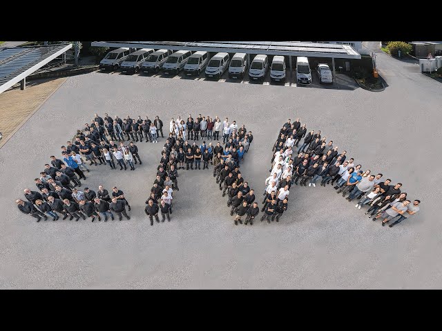 meinkarrierestart.at Eine große Gruppe von Menschen steht in Formation auf dem Bürgersteig und bildet die Form eines Pfeils, der nach rechts zeigt. Im Hintergrund sind mehrere Fahrzeuge geparkt.