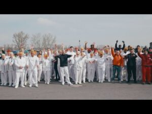 meinkarrierestart.at Eine große Gruppe von Menschen, meist in weißen Uniformen, steht im Freien, einige heben die Arme und winken, im Hintergrund sind Bäume und der Himmel zu sehen.