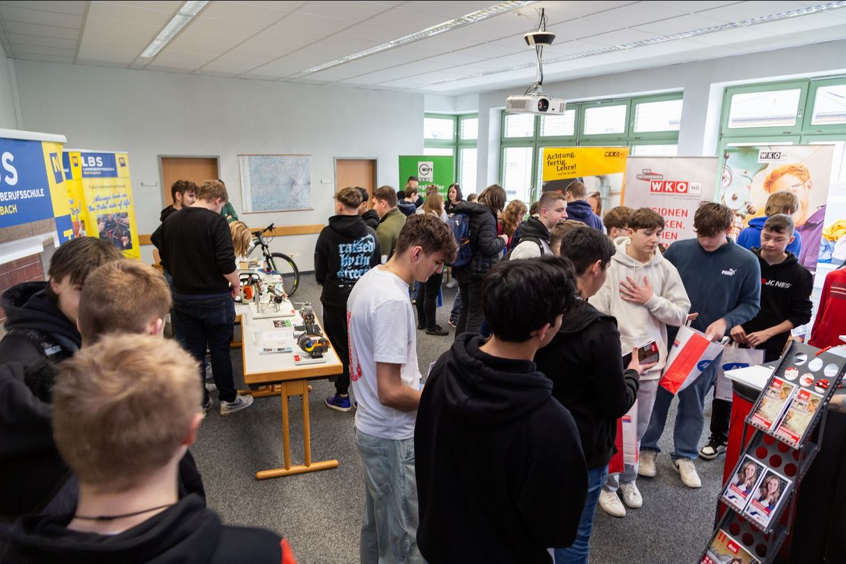 meinkarrierestart.at Eine Gruppe von Schülern besucht verschiedene Stände auf einer überdachten Berufs- oder Bildungsmesse, spricht mit den Ausstellern und sammelt Informationsmaterial.